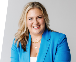 Portrait of a smiling woman with blonde hair wearing a blue blazer and gold necklace.